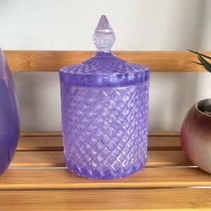 May include: A purple glass candle jar with a diamond pattern and a clear glass lid with a pointed top.