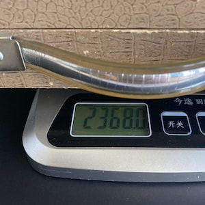 May include: A digital kitchen scale displays a weight of 2368.0. The scale is silver and black, with a digital display. A brown textured surface and a silver handle are visible in the background.