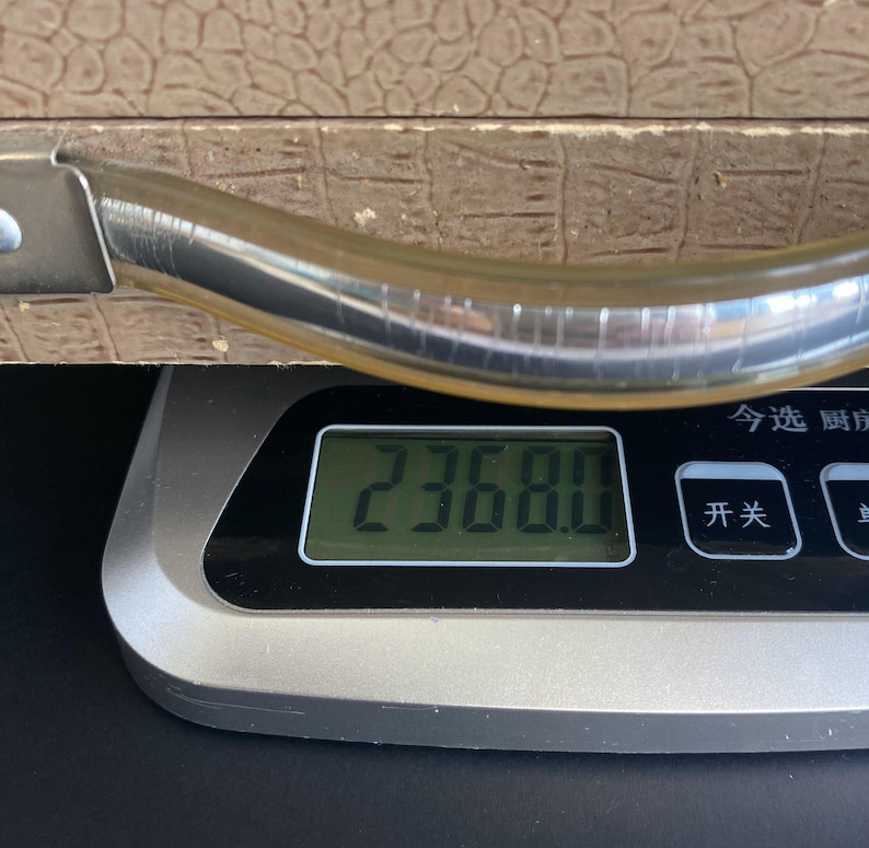 May include: A digital kitchen scale displays a weight of 2368.0. The scale is silver and black, with a digital display. A brown textured surface and a silver handle are visible in the background.
