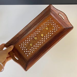 May include: A rectangular wooden tray with a dark brown finish. The tray features a decorative inlaid design of white dots and gold-colored leaf shapes. It has curved edges and handles for easy carrying.