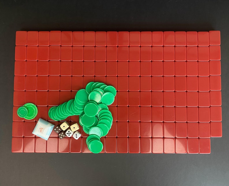 May include: A red rectangular game board with a grid of red tiles. Green circular game pieces and dice are scattered across the board. A small white pouch is also present. The game pieces are in a variety of shapes and sizes.