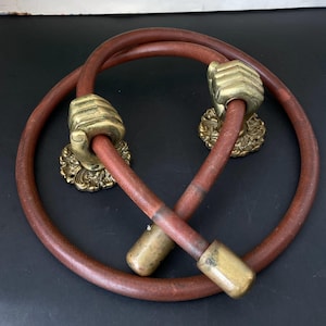 Könnte beinhalten: Ein Paar Vintage-Türgriffe aus braunem Leder und Messing. Die Griffe haben messingfarbene, faustförmige Griffe, die an einem gebogenen Lederrohr befestigt sind. Die Messingelemente haben eine gealterte Patina, und das Leder ist rotbraun.