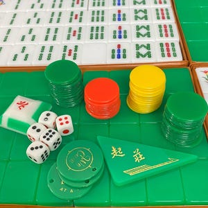 May include: A Mahjong set with white tiles, green and blue symbols, dice, and coloured chips. The set includes green, red, and yellow chips, a green triangular marker and dice.