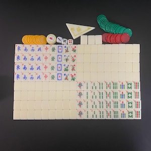 May include: A complete Mahjong set with ivory-coloured tiles, dice, and colourful chips. The tiles feature Chinese characters and symbols in blue, red, and green. The set includes a white triangular wind indicator.
