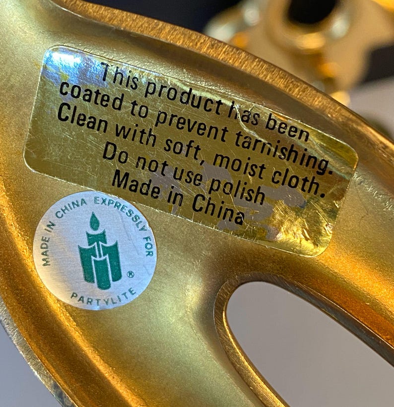 May include: Close-up of a gold-colored metal decorative object with a sticker that reads "This product has been coated to prevent tarnishing. Clean with soft, moist cloth. Do not use polish. Made in China."