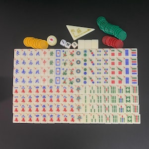 May include: A complete Mahjong set with ivory-coloured tiles, dice, and coloured chips. The tiles feature Chinese characters and symbols in red, green, and blue. The set includes green, red, and yellow chips, and a white triangular piece.
