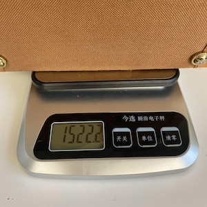 May include: A brown bag is placed on a digital kitchen scale. The scale displays a weight of 1522.2. The scale has a black display with Chinese characters and buttons.