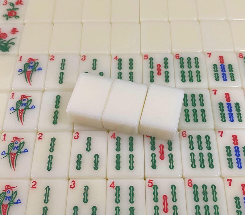 May include: A close-up of a Mahjong set with ivory-coloured tiles. Three tiles are in focus, with the numbers 3, 4, and 5 visible. The other tiles have green, red, and blue symbols and numbers.