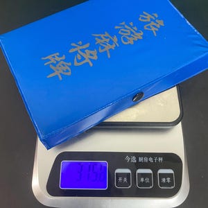 Puede incluir: Una caja azul de fichas de Mahjong con letras doradas descansa sobre una b&aacute;scula de cocina digital. La b&aacute;scula muestra un peso de 375,8. La b&aacute;scula tiene botones con caracteres chinos.