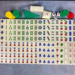 May include: A complete Mahjong set with ivory-colored tiles featuring Chinese characters and symbols. Includes green, red, and yellow chips, dice, and a green triangular wind indicator. A classic game.
