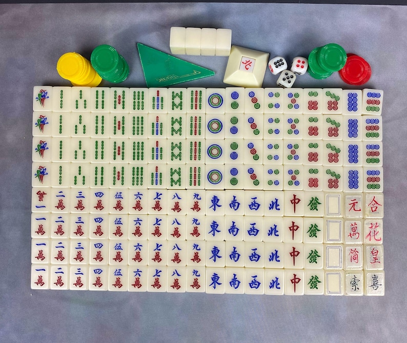 May include: A complete Mahjong set with ivory-colored tiles featuring Chinese characters and symbols. Includes green, red, and yellow chips, dice, and a green triangular wind indicator. A classic game.