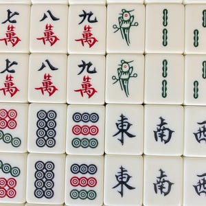 Puede incluir: Primer plano de una colecci&oacute;n de fichas de Mahjong blancas. Las fichas presentan varios s&iacute;mbolos y caracteres chinos en rojo, verde y negro. Algunas fichas muestran conjuntos de c&iacute;rculos, otras caracteres chinos.