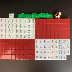Puede incluir: Un juego de Mahjong completo dispuesto sobre una superficie negra. El juego incluye fichas rojas y blancas, fichas verdes y dados. Las fichas están marcadas con caracteres y símbolos chinos.