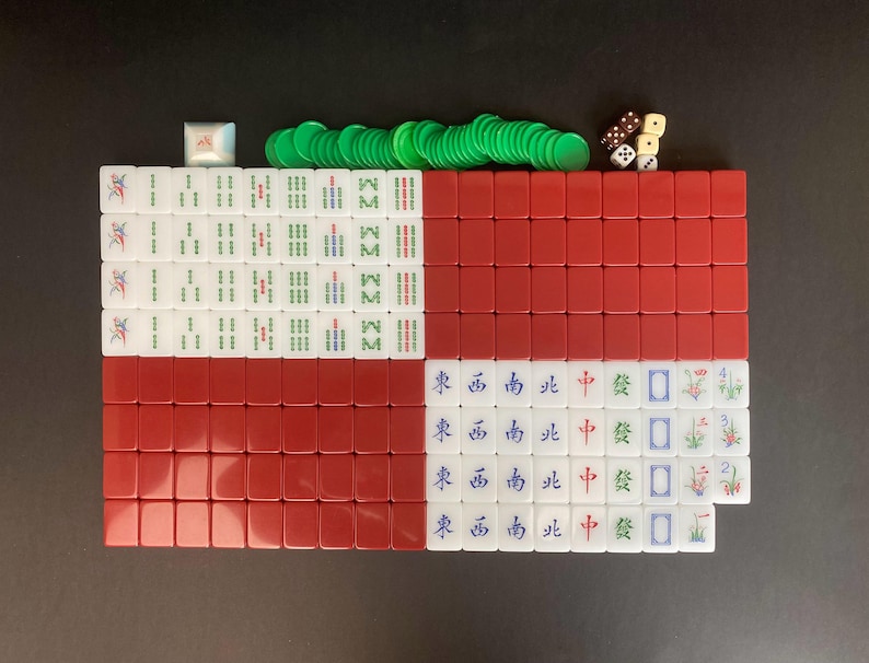 May include: A complete Mahjong set arranged on a black surface. The set includes red and white tiles, green chips, and dice. The tiles are marked with Chinese characters and symbols, perfect for game night.