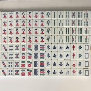 Puede incluir: Un juego completo de fichas de Mahjong blancas con marcas rojas, verdes y azules. Las fichas est&aacute;n dispuestas sobre una superficie blanca, con dos dados y un dado amarillo. El juego incluye fichas con caracteres y s&iacute;mbolos chinos.