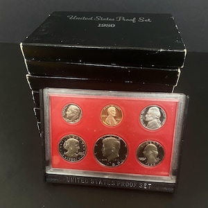 May include: A 1980 United States Proof Set in a black box. The set contains six coins displayed on a red background. The coins feature portraits of historical figures and the text "United States Proof Set 1980".