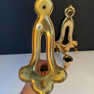 May include: Two vintage brass candle holders. The candle holders have a decorative, ornate design with a curved shape and a small cup for the candle. The brass has a shiny, polished finish. The text on the sticker says "This product is coated to prevent tarnishing. Clean with soft, mold cloth. Made in China."