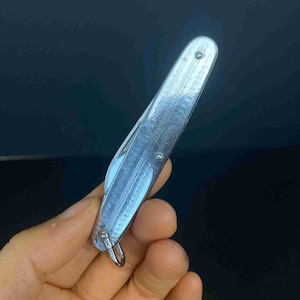 May include: A silver-toned folding pocket knife featuring a textured handle with a repeating wavy line pattern. The handle has a metallic finish and includes a small metal loop at the base for attachment. The knife is closed, showing the exterior casing.