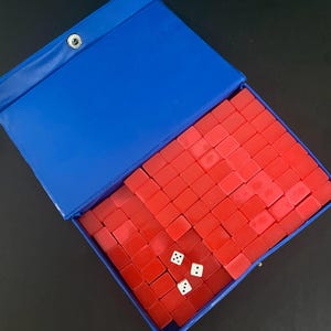 Puede incluir: Un estuche azul abierto que contiene un juego de fichas rojas y tres dados blancos. Las fichas est&aacute;n cuidadosamente dispuestas. El estuche tiene un cierre a presi&oacute;n. Un juego cl&aacute;sico.