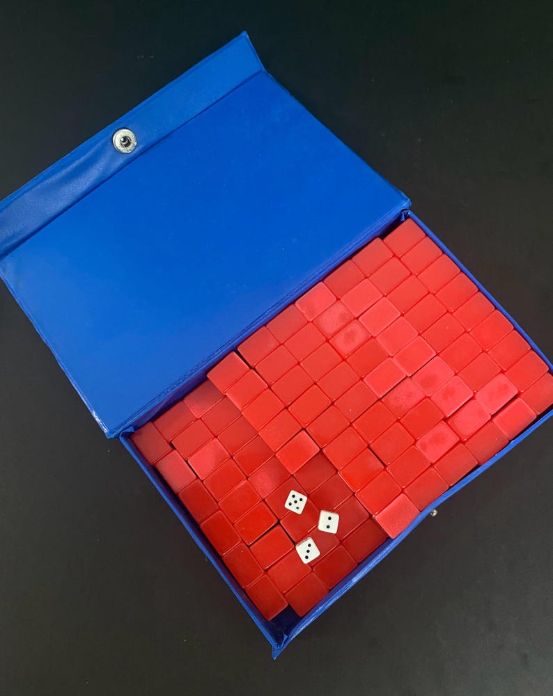 Puede incluir: Un estuche azul abierto que contiene un juego de fichas rojas y tres dados blancos. Las fichas est&aacute;n cuidadosamente dispuestas. El estuche tiene un cierre a presi&oacute;n. Un juego cl&aacute;sico.