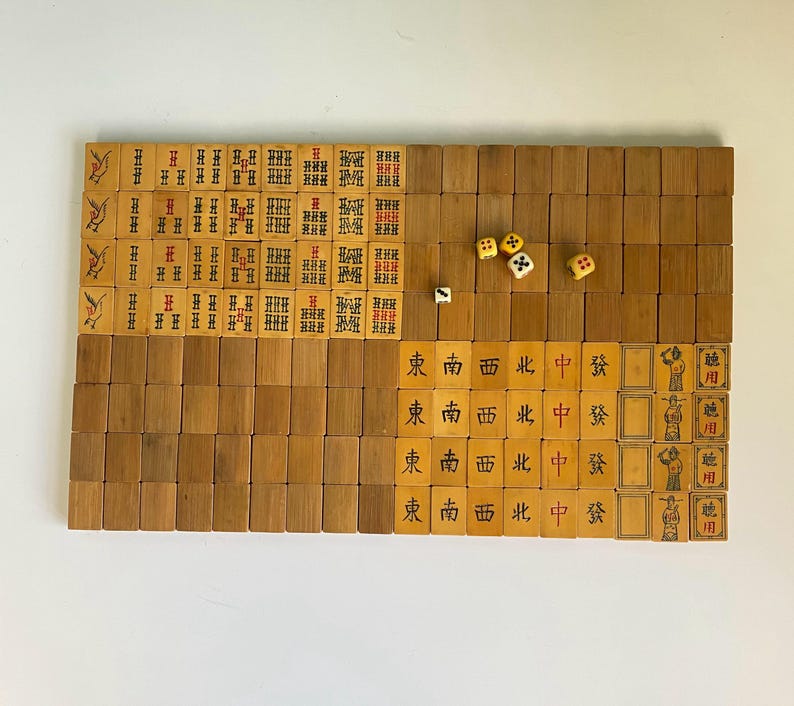 May include: A vintage Mahjong set with wooden tiles and dice. The tiles feature Chinese characters and symbols in red and black ink. The set is arranged on a white surface, showcasing the game's components.