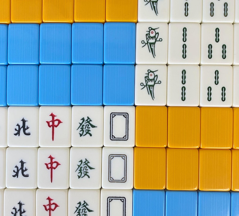 Puede incluir: Vista a&eacute;rea de fichas de Mahjong dispuestas en una cuadr&iacute;cula. Las fichas muestran varios s&iacute;mbolos, caracteres y colores, incluyendo azul, amarillo y blanco. Algunas fichas presentan caracteres chinos.