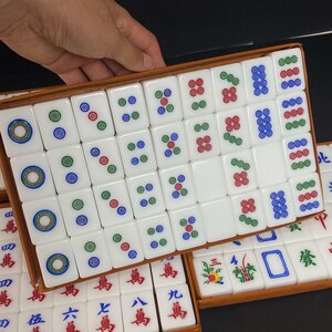 May include: A set of white Mahjong tiles with colourful markings, including circles and symbols in red, green, and blue. The tiles are arranged in a wooden box, with some tiles visible in a second box below.