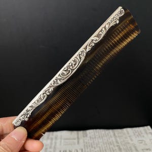 May include: A brown tortoiseshell comb with a silver, ornate, decorative handle.