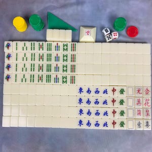 May include: A complete Mahjong set with ivory-colored tiles, dice, and chips. The tiles feature Chinese characters and symbols in red, green, and blue. Additional components include green and yellow chips, and a green triangle.