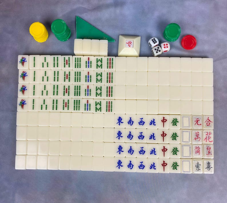 May include: A complete Mahjong set with ivory-colored tiles, dice, and chips. The tiles feature Chinese characters and symbols in red, green, and blue. Additional components include green and yellow chips, and a green triangle.
