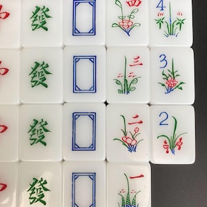 May include: A collection of white Mahjong tiles with various symbols and characters. Some tiles feature green Chinese characters, blue rectangles, and red and green floral designs. Numbers 2, 3, and 4 are also visible on some tiles.