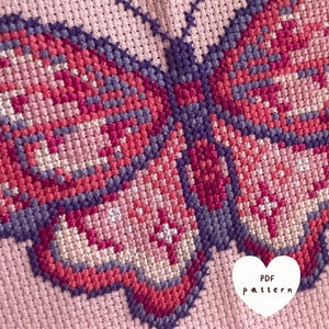 Op de afbeelding: Een kruissteekpatroon van een vlinder met roze, paarse en witte draad op een roze stoffen achtergrond. De tekst "PDF pattern" staat in een wit hartje in de rechterbenedenhoek.