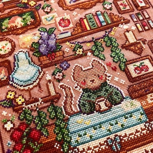 May include: A detailed cross-stitch design featuring a cozy scene with a cat holding a mug, surrounded by bookshelves, framed pictures, and floral accents. The color palette includes shades of brown, green, blue, and pink, creating a warm and inviting aesthetic.