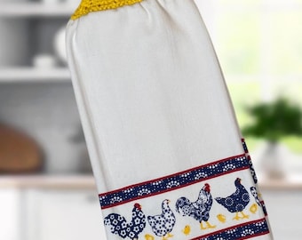 Op de afbeelding: Witte keukendoek met een blauw en wit kippenpatroon en een gele gehaakte ophanglus met een blauwe knoop.