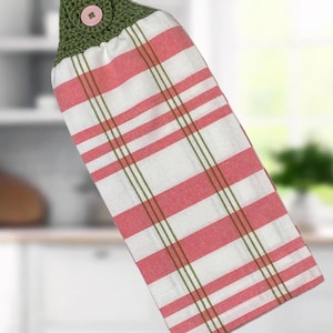 May include: A hanging kitchen towel with a red and white striped pattern. The top portion is a crocheted green fabric with a pink button closure. The towel has a classic, farmhouse style.