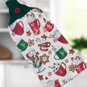 Peut inclure: Un torchon de cuisine blanc avec un dessus crocheté vert et un bouton rouge. Le torchon présente un motif festif de tasses rouges et vertes, de biscuits en pain d'épices et de cannes en bonbon. Le texte "2-en-1 fonctionnalité !" est visible.