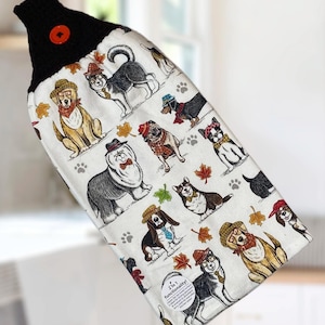 May include: A white kitchen towel with a black top and a red button. The towel is patterned with various dog breeds wearing hats and scarves. The text "2 in 1 functionality!" is visible.