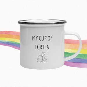 May include: White enamel mug with a black rim and handle. The mug features the text "MY CUP OF LGBTEA" in black, along with a small illustration of a tea bag. A watercolor rainbow is in the background.