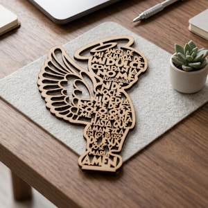 Puede incluir: Una silueta de ángel de madera cortada con láser que presenta un intrincado diseño calado de la oración Angel de mi guarda. El texto forma el cuerpo y las alas del ángel, terminando con la palabra Amen en la base, mostrando gran detalle.