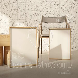 May include: Two wooden picture frames with blank white canvases, standing on a light gray floor. A brown chair is in the background against a white and gray speckled wall.