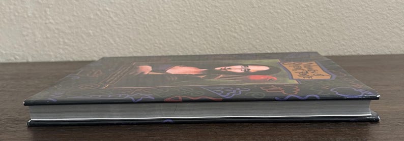 K&ouml;nnte beinhalten: Eine wei&szlig;e Keramik-Tasse mit schwarzem Henkel und dem Text "But First, Coffee" in fetter, schwarzer Schrift. Die Tasse steht vor einem verschwommenen Hintergrund, der eine gem&uuml;tliche Umgebung suggeriert.