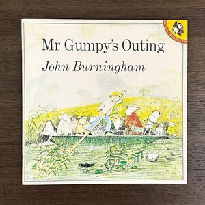 May include: A square children's picture book titled Mr Gumpy's Outing by John Burningham. The cover features a watercolor illustration of a person in a boat with various animals and children on a river, with a yellow Picture Puffin logo in the corner.