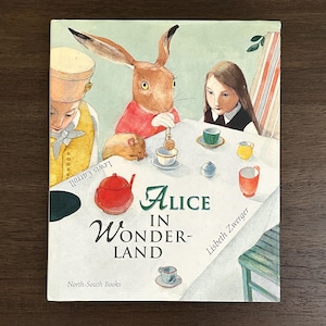 May include: A hardcover book titled "Alice in Wonderland" with illustrations. The cover features a watercolor painting of a rabbit, a girl, and other characters around a table. The book is published by North-South Books.