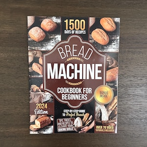 May include: A softcover cookbook titled Bread Machine Cookbook for Beginners 2024 Edition. The cover features various baked bread loaves, a brown decorative frame, and text highlighting 1500 days of recipes, a bonus inside, and over 70 video tutorials included.