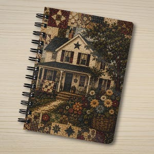May include: A spiral-bound notebook featuring a cover with a patchwork quilt pattern border and a central illustration of a two-story house with a front porch, a star emblem on the gable, and baskets of colorful flowers in the front yard.