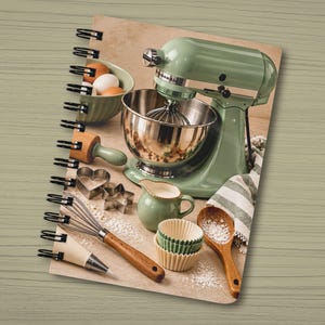 May include: A spiral-bound notebook featuring a cover image of a sage green stand mixer, a bowl of eggs, a rolling pin, heart and star cookie cutters, a whisk, a piping bag, a small pitcher, paper cupcake liners, and a wooden spoon.