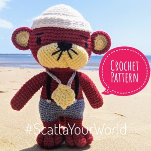 Puede incluir: Muñeco de mono de ganchillo hecho a mano con cuerpo rojo, cara amarilla y gorro blanco. El mono lleva pantalones cortos grises, tirantes negros y un colgante amarillo. Incluye el texto "CROCHET PATTERN" y "#ScattaYourWorld".