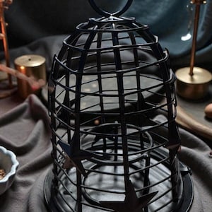 May include: Black metal candle lantern with a cage design and star accents. The lantern has a round base and a handle at the top. Decorative item for home decor, suitable for candles or small lights.