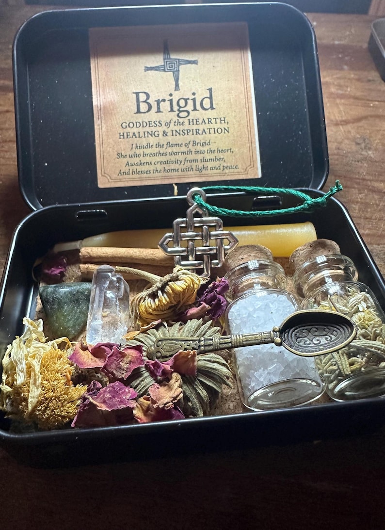 Puede incluir: Una caja de metal negro que contiene un kit de altar de Brigid. El kit incluye una tarjeta con texto, cristales, flores secas, velas, peque&ntilde;os frascos de vidrio y una cuchara decorativa. El texto de la tarjeta dice "Brigid, Diosa del Hogar, la Curaci&oacute;n y la Inspiraci&oacute;n."