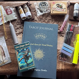 May include: A collection of spiritual items on a wooden surface. Includes a tarot journal, a Van Gogh Tarot deck, incense cones, a crystal, tea bags, a candle, pens, stickers, and small jars with dried herbs. The journal reads "Tarot Journal".